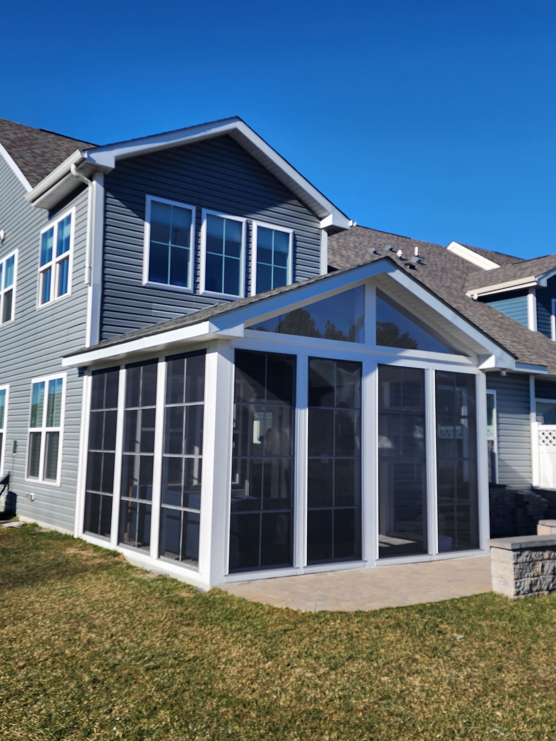 Screened porch addition to a house with blue siding, gray roof, and a clear blue sky.