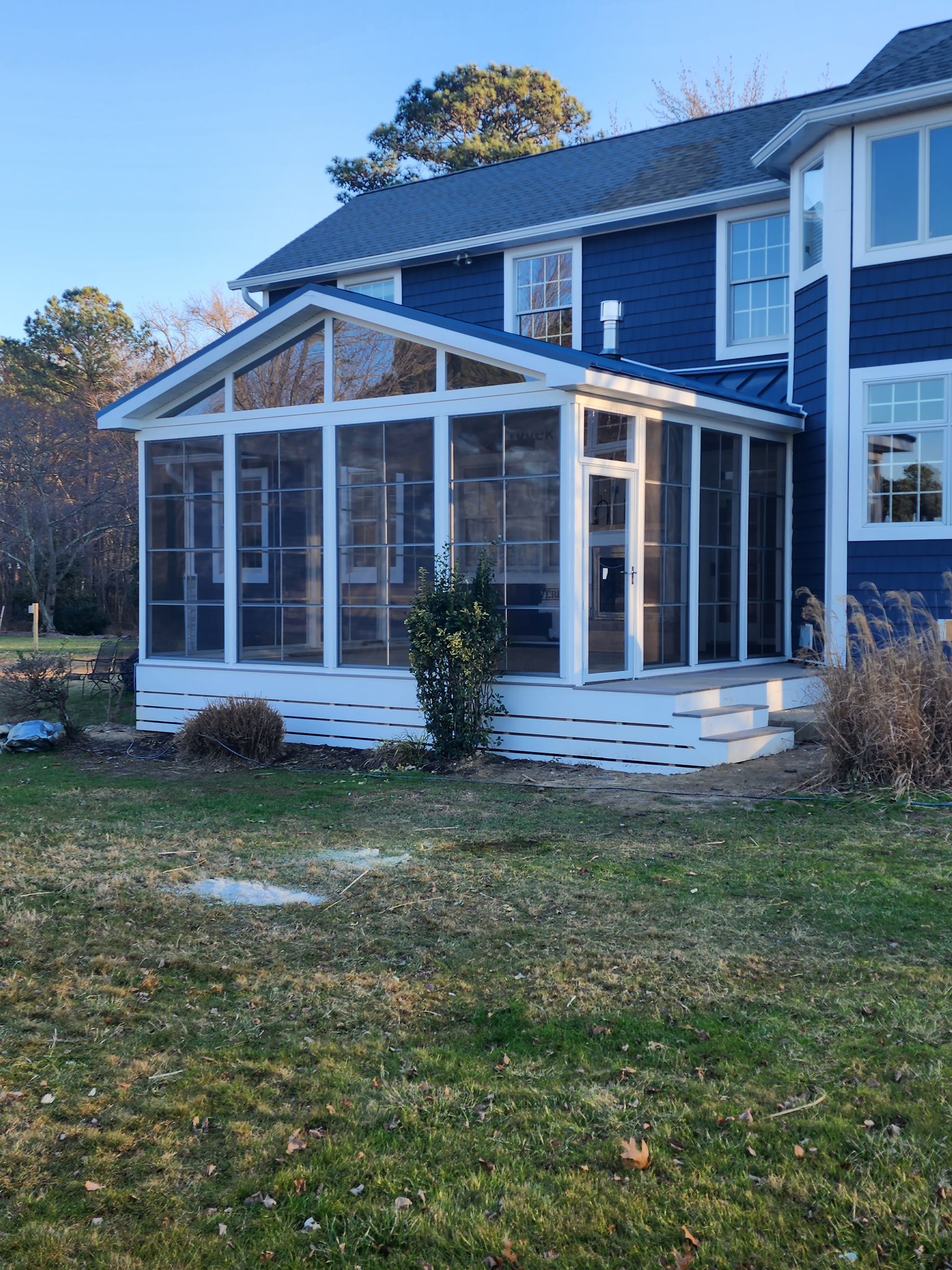Blue house with a white screened porch and surrounding green grass.