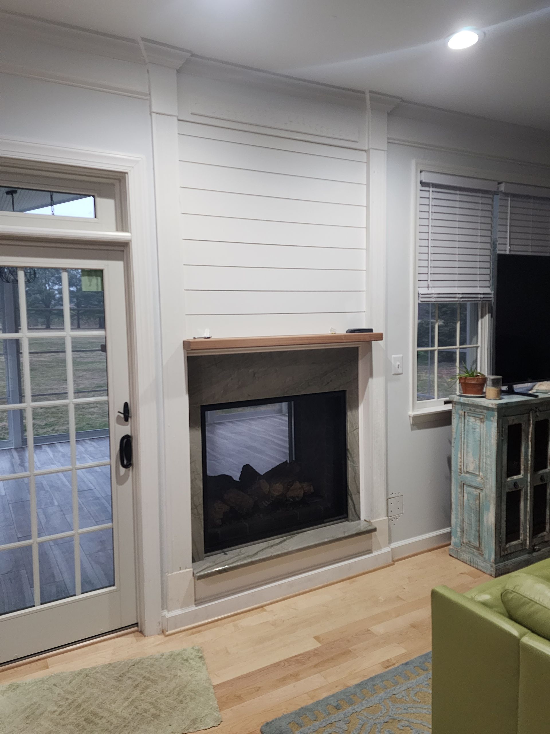 Fireplace with wooden mantel and shiplap accent wall. A door and window are nearby.