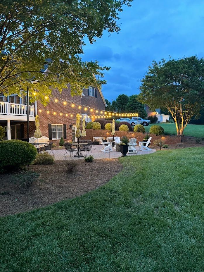 Backyard patio at dusk with string lights, seating, and landscaping.