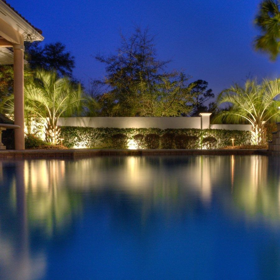 Nighttime pool with illuminated landscaping and reflections.