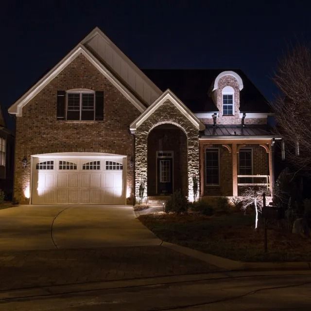 Well-lit brick house at night with a two-car garage, porch, and driveway.