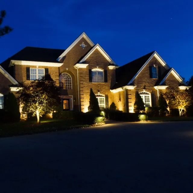 A large brick house illuminated at night with outdoor lighting.
