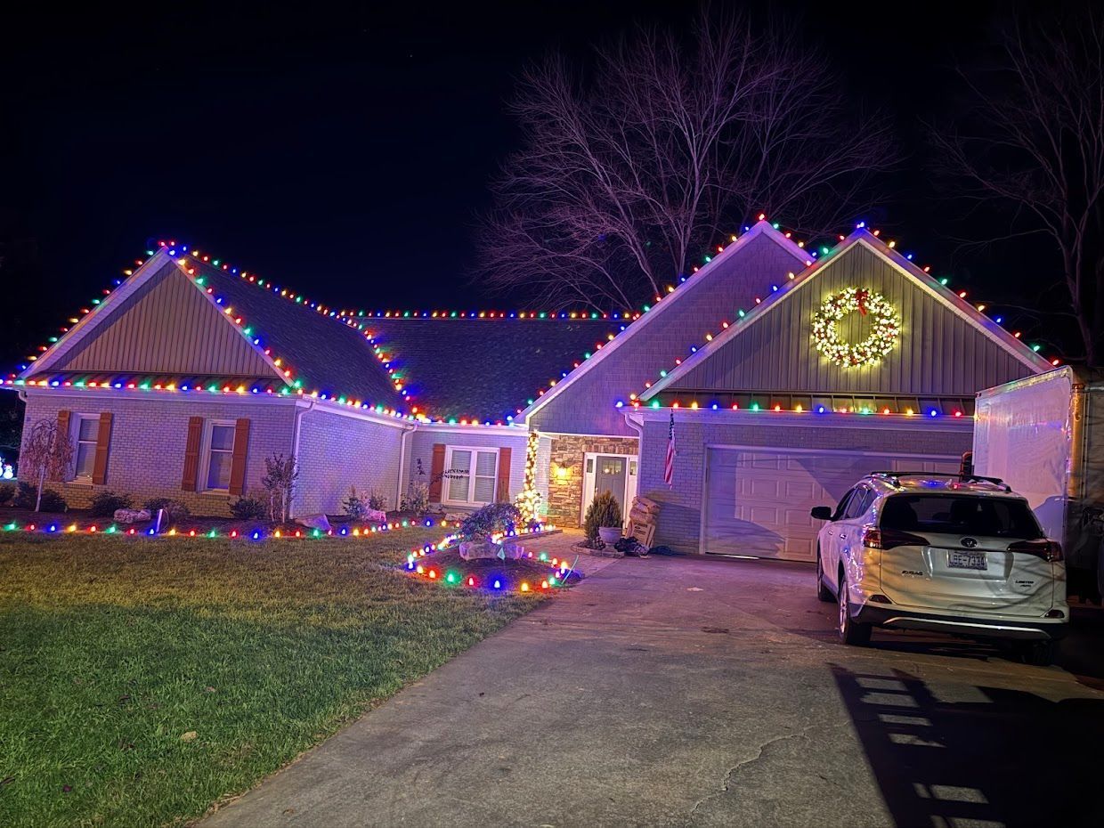 House decorated with colorful Christmas lights at night, a wreath on the garage door.