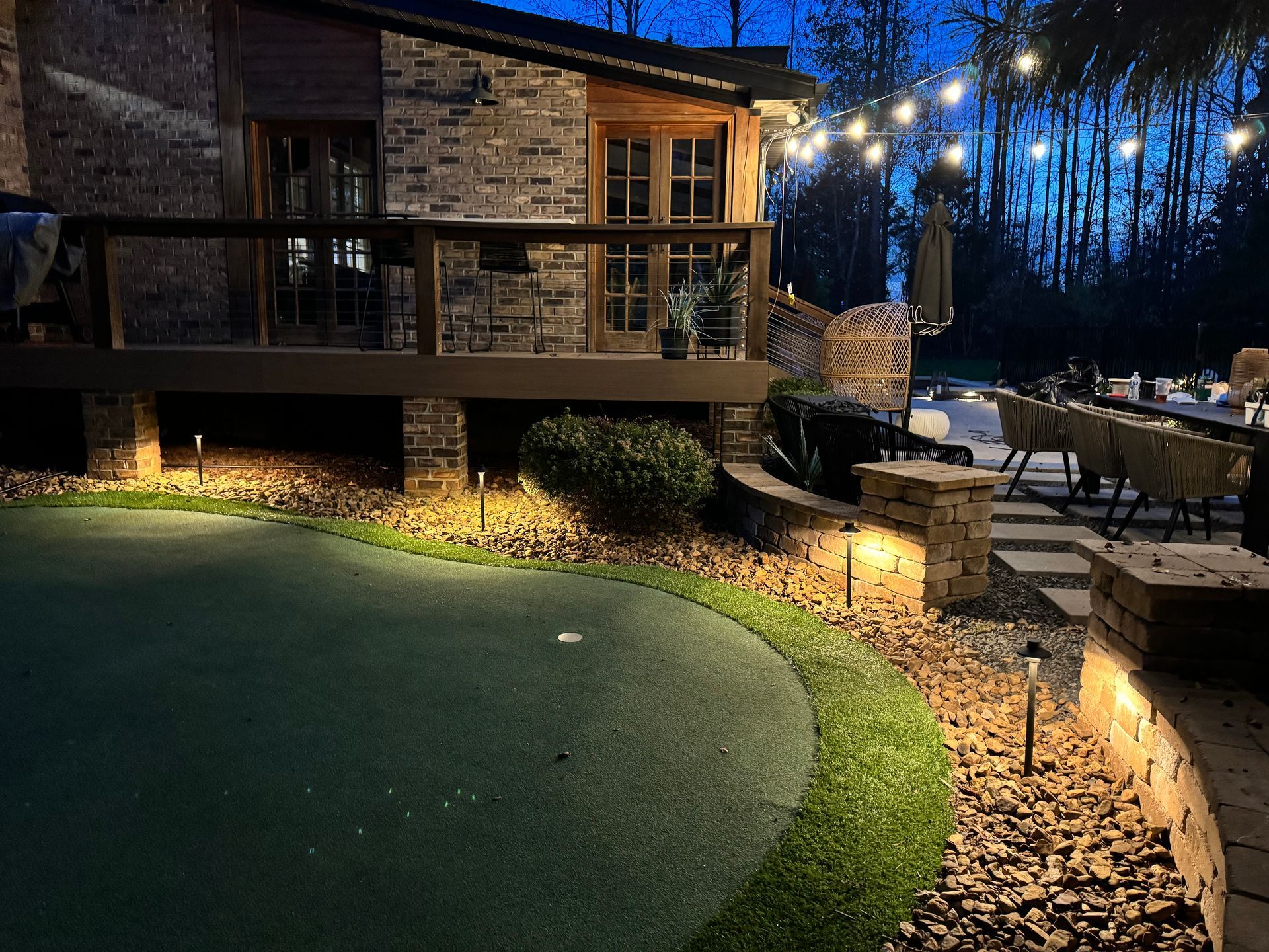 Nighttime backyard scene with lit home, golf green, and string lights.