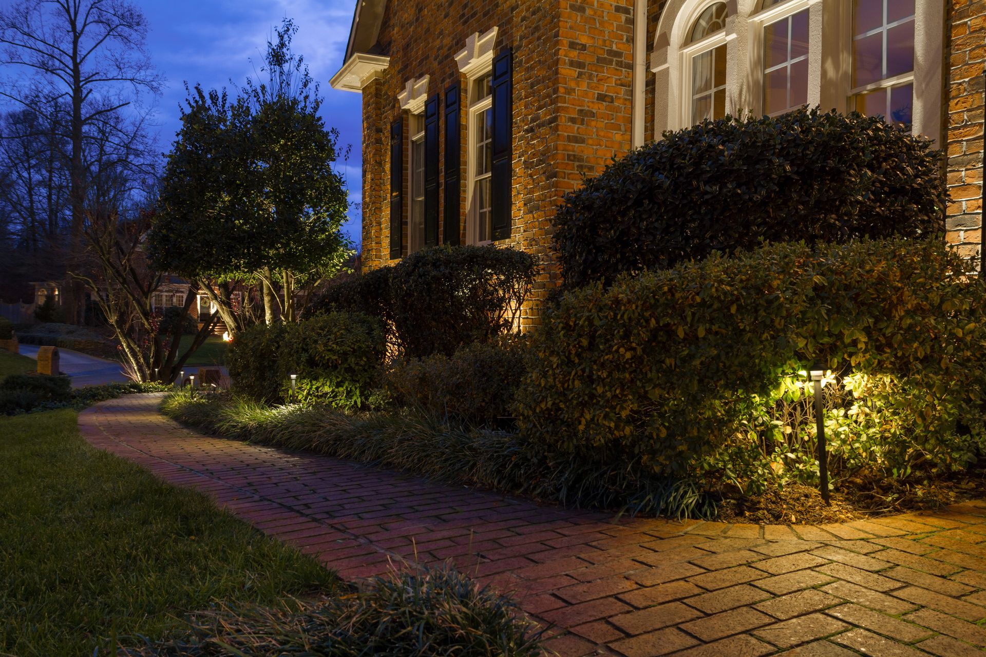 Brick path and landscaping illuminated by lights at night, leading to a brick home.