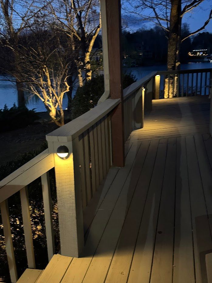 Lit deck railing at dusk, overlooking a lake. Warm lights cast shadows on the wood.