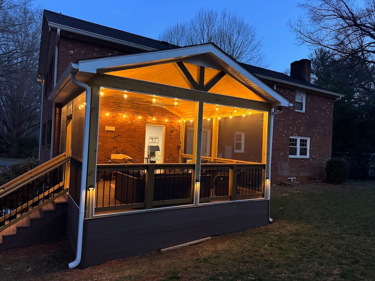 Screened porch with string lights attached to a brick house at dusk.