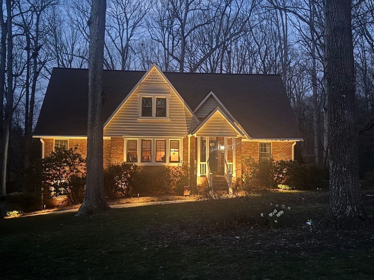 Cozy brick house at dusk, lit with warm exterior lights. Trees frame the property.
