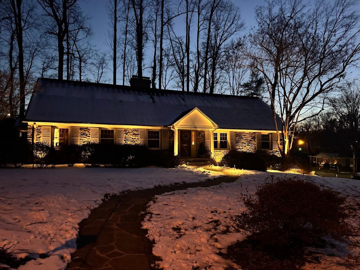 Stone house at dusk with illuminated facade, snow-covered yard, and stone path leading to the entrance.