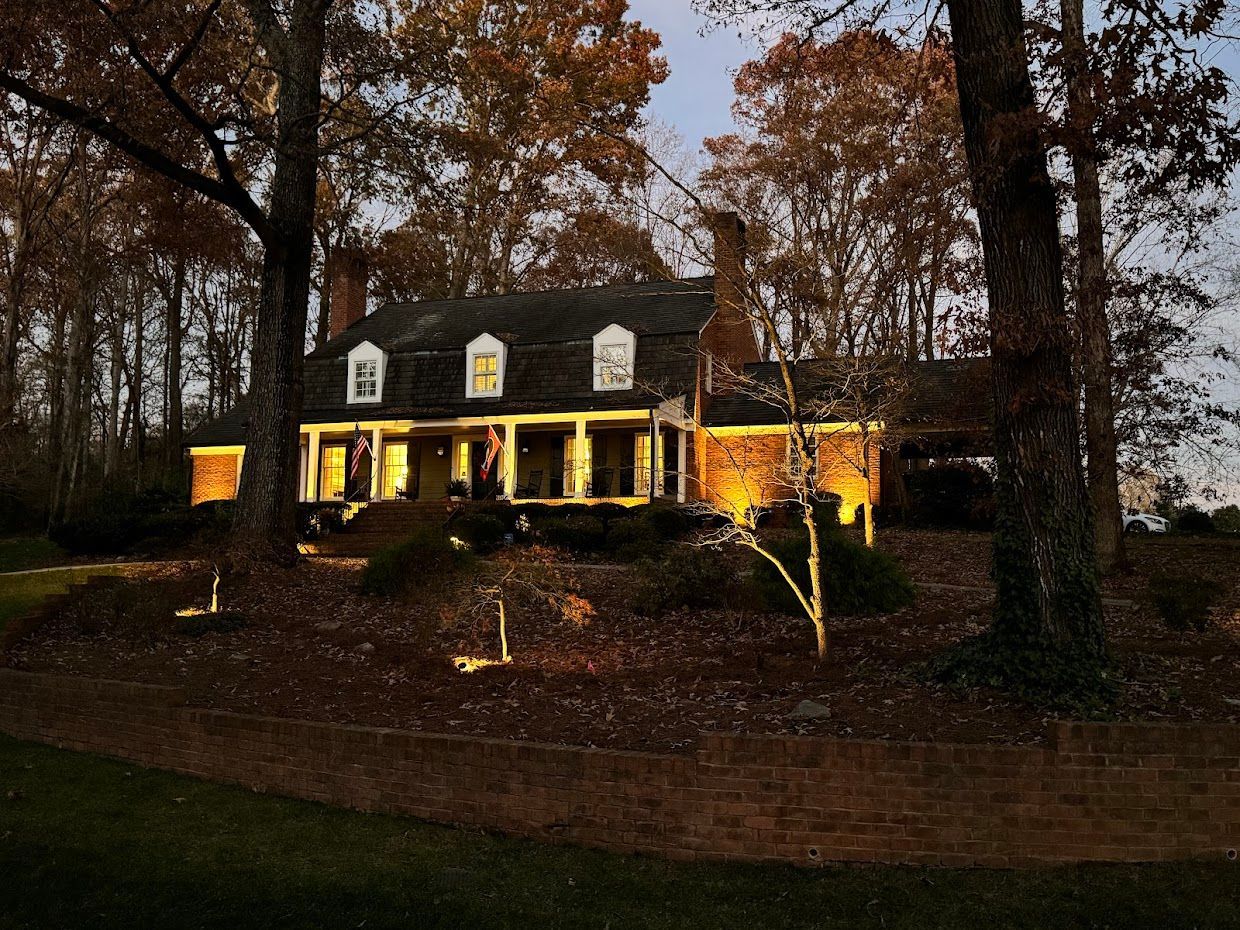 Colonial-style house illuminated by warm lights, set among trees during dusk.