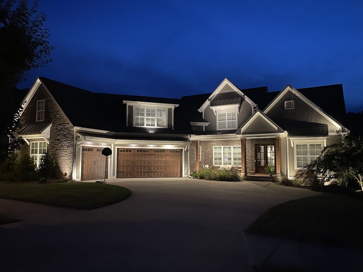 A large house at night with illuminated landscaping and exterior lights.
