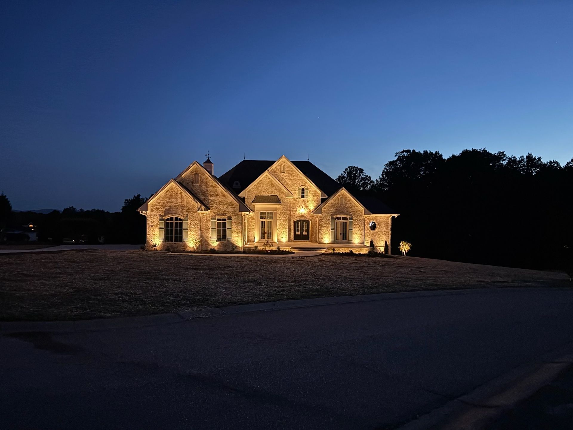 A stone-faced house illuminated by exterior lights at dusk against a dark blue sky.