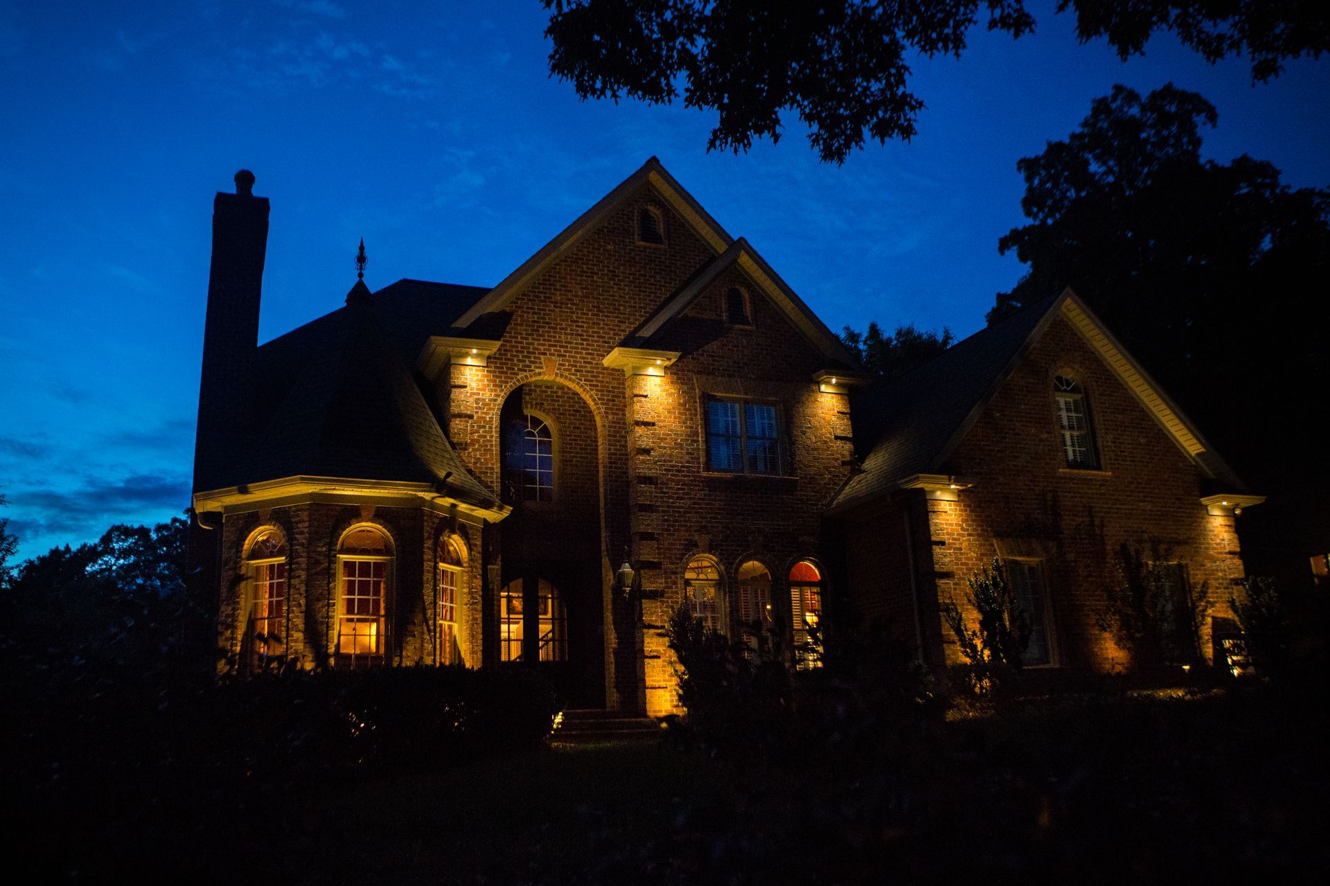 A brick house illuminated by golden outdoor lights at dusk, showcasing architectural details.
