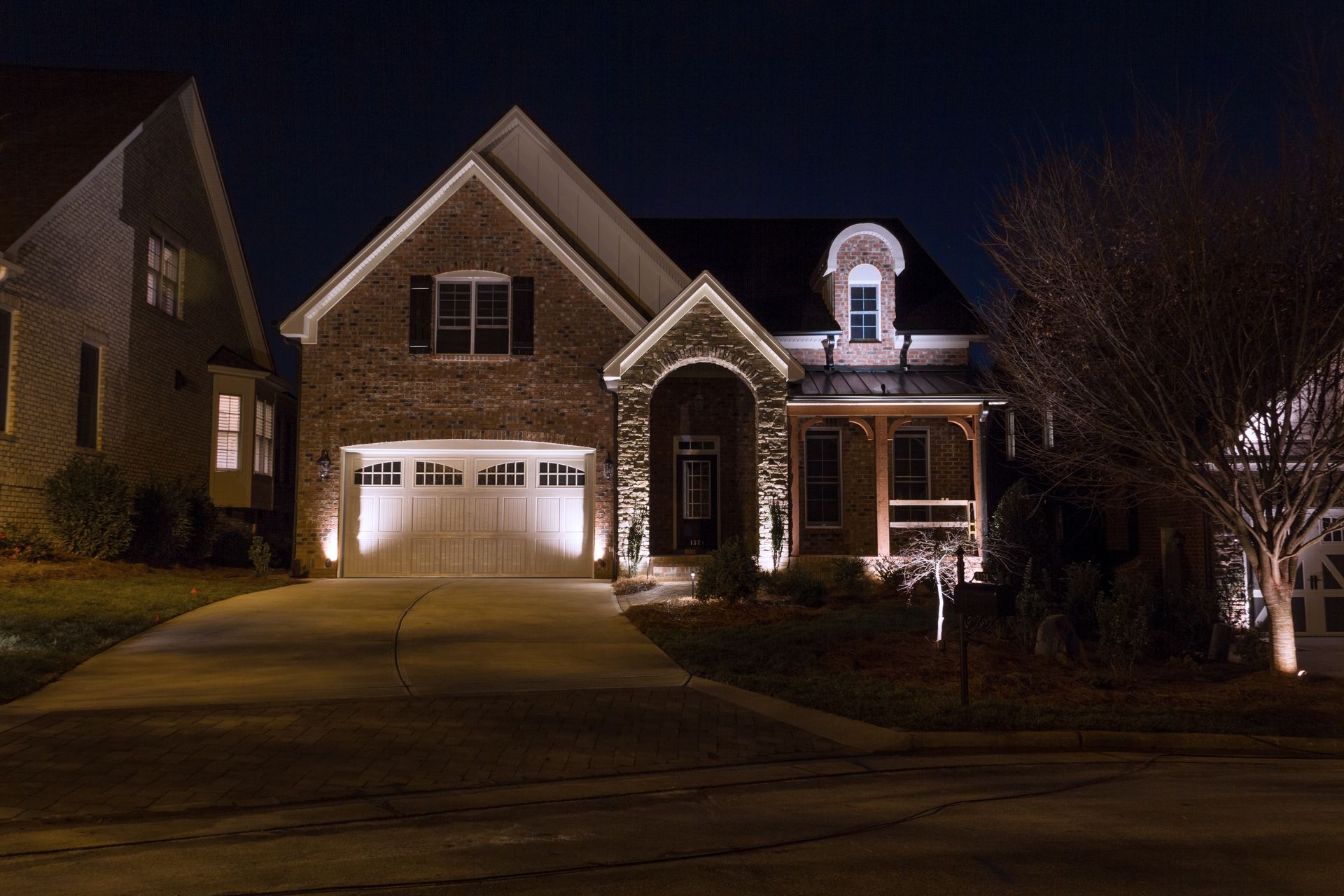 Illuminated house at night with spotlighting on the facade, driveway, and porch.