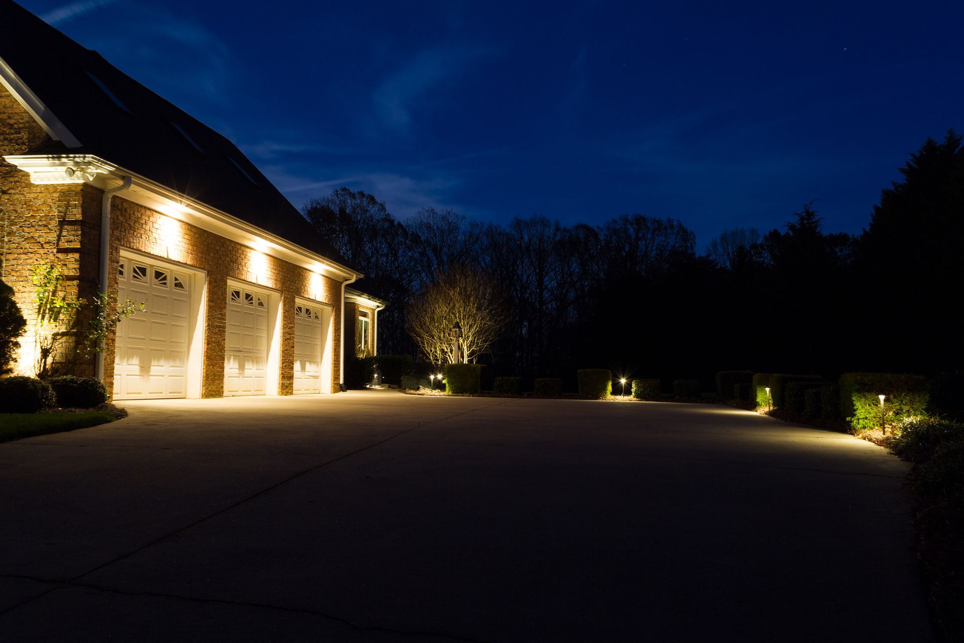 A house with illuminated garage doors and driveway at night.