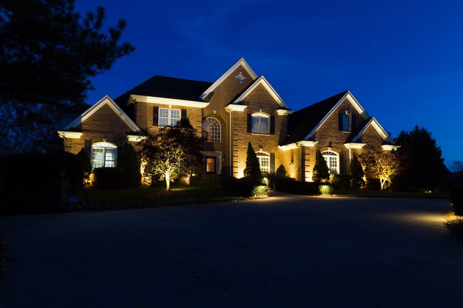 Large brick house illuminated at night with landscape lighting.