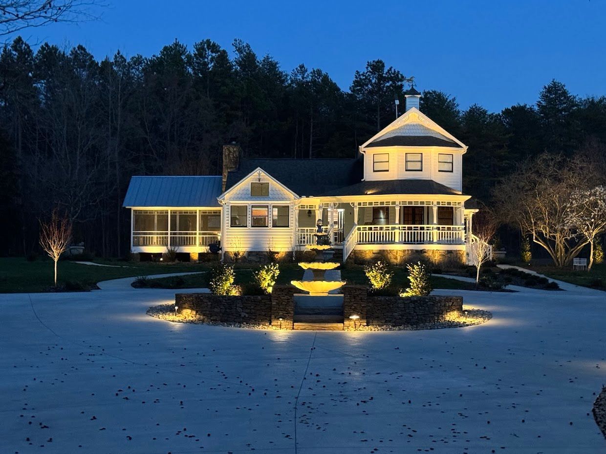 A white house illuminated at night with a well-lit stone pathway leading to the entrance. Dark trees in the background.