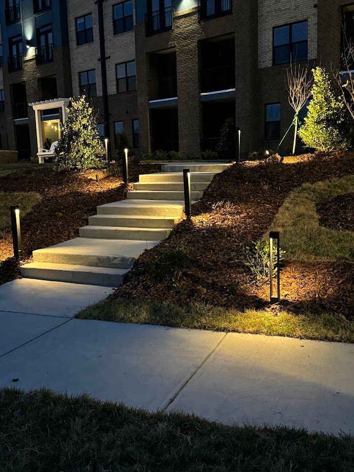 Exterior staircase with pathway lights leading to an apartment building at dusk. Mulched landscaping on either side.