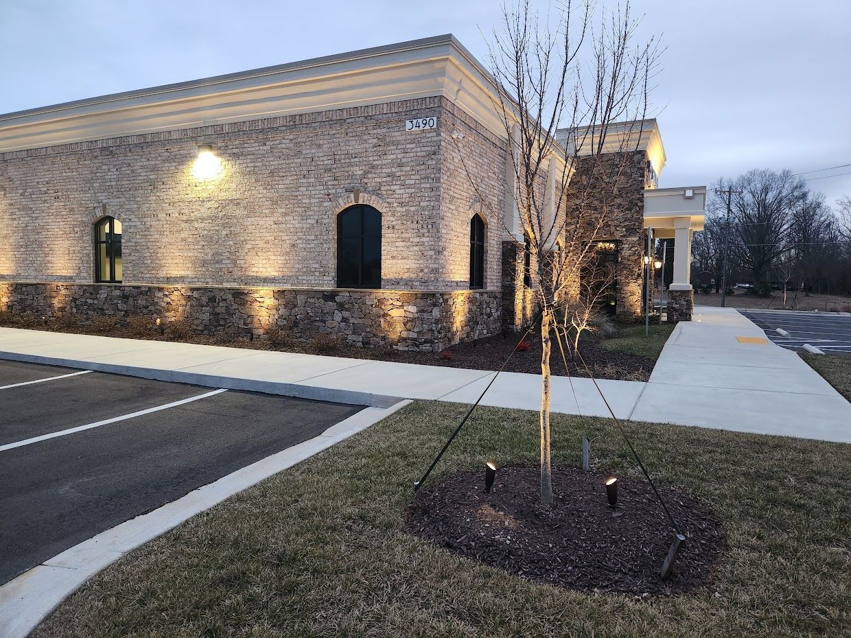 Brick building with arched windows, exterior lighting, small tree in front, sidewalk, asphalt.