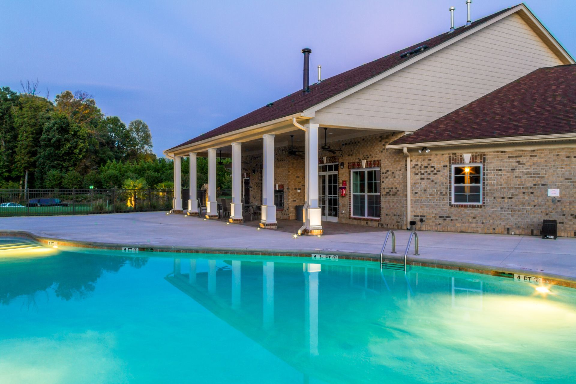 Pool with clear water, adjacent to a building with columns and a brick exterior, at dusk.