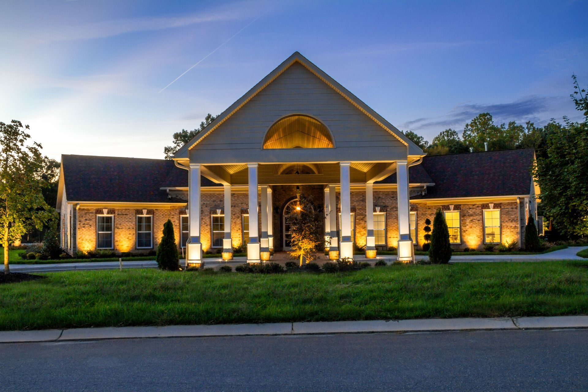 Elegant building with pillars illuminated at night, featuring a brick facade and manicured lawn.