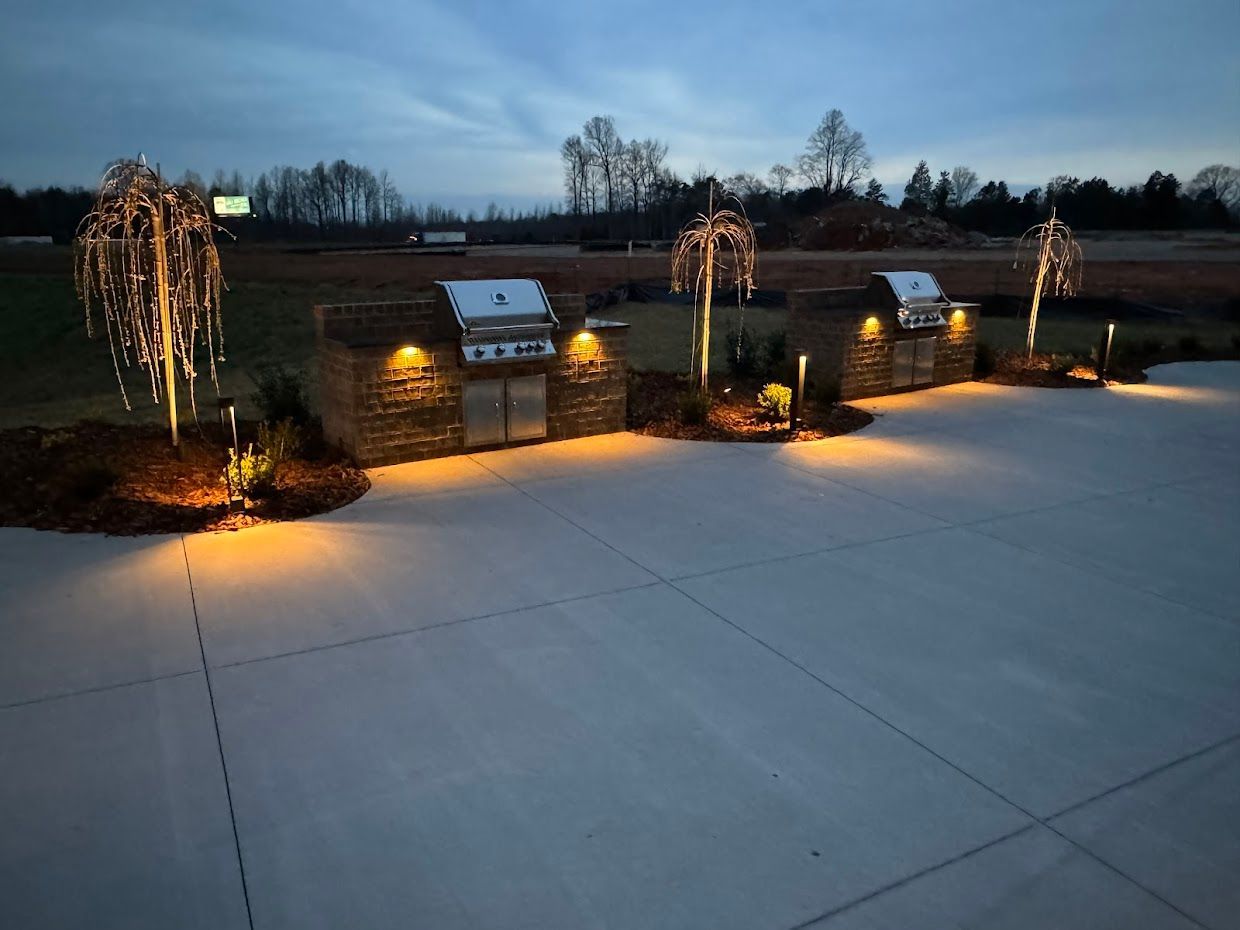 Outdoor kitchen with two grills, lit with warm lights against a twilight sky.