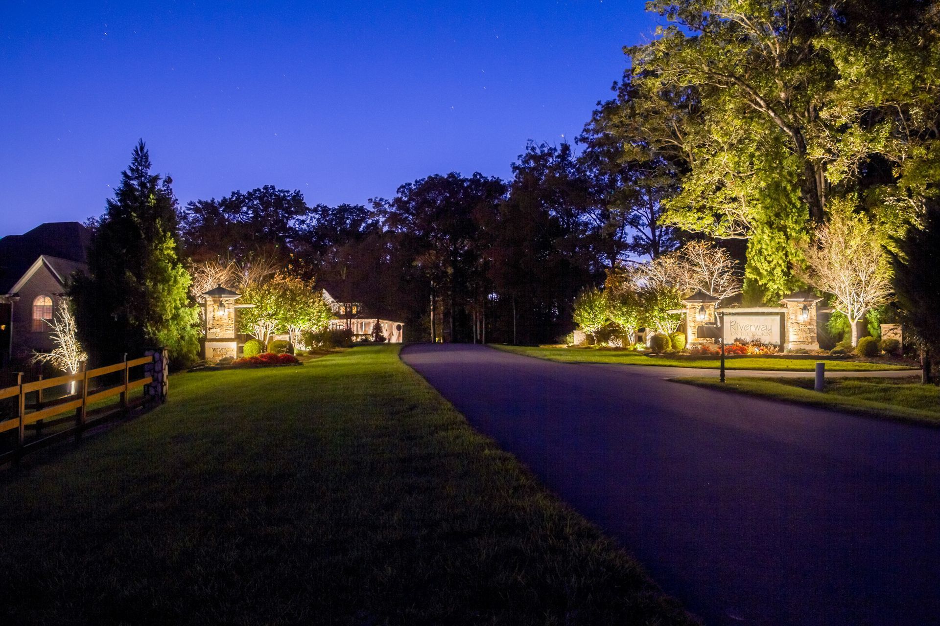 Nighttime street entrance lit by outdoor lights with landscaped trees and lawns.