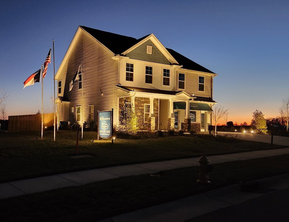 Two-story house with illuminated exterior at dusk. Flags fly out front, dusk sky in the background.