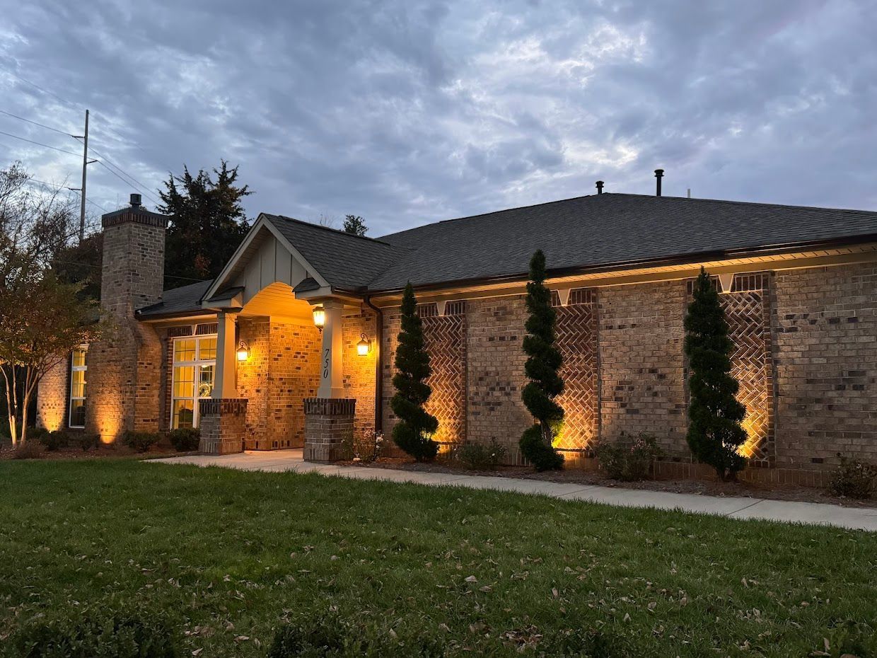Brick building with exterior lighting, landscaping, and cloudy sky.