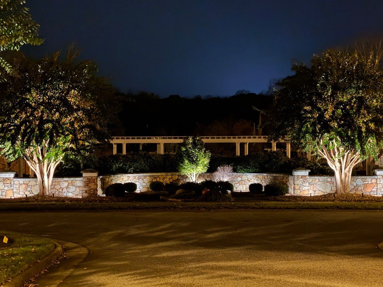 Night view of a stone wall, illuminated trees, and a structure under a dark sky.