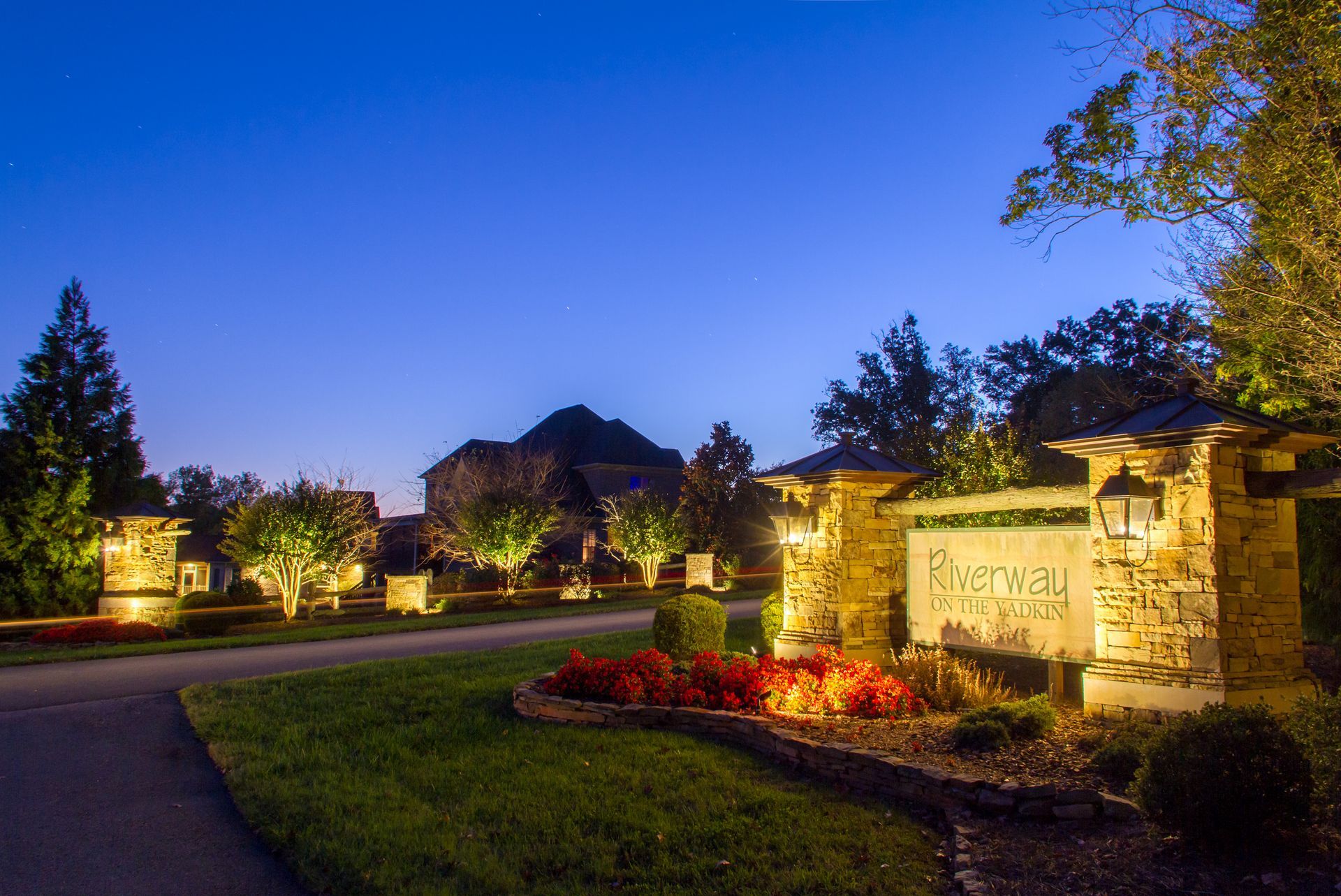 Night view of a stone entrance with illuminated signage and landscaping, blue sky.