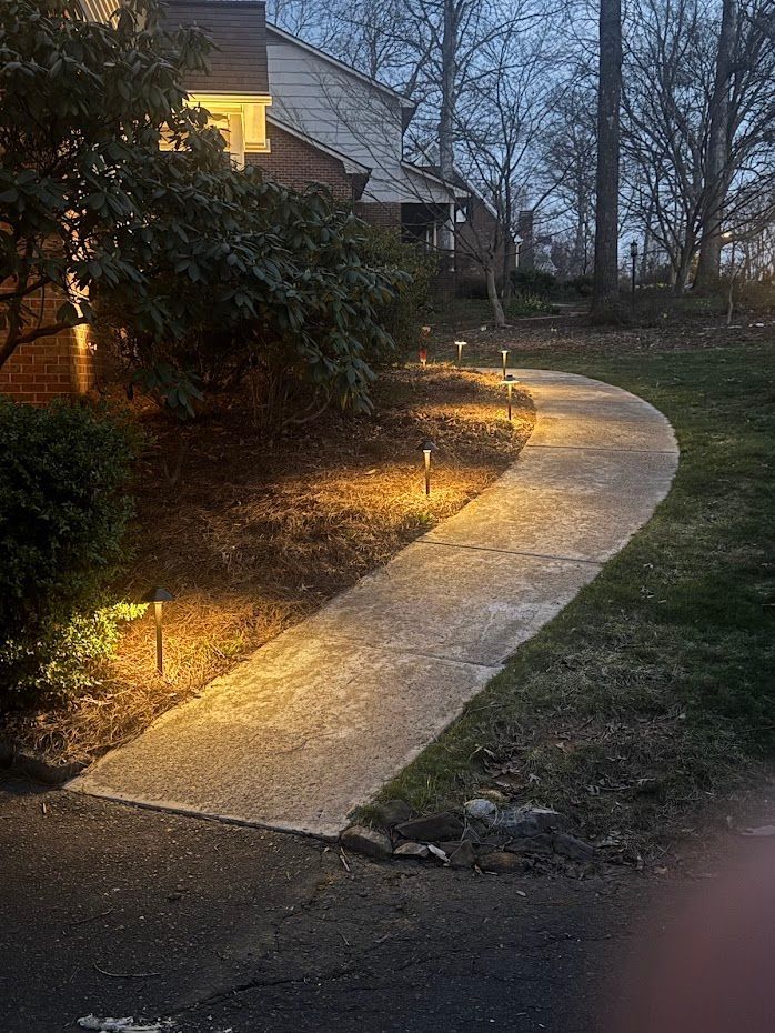 Pathway illuminated by lights at dusk, leading through a grassy yard.