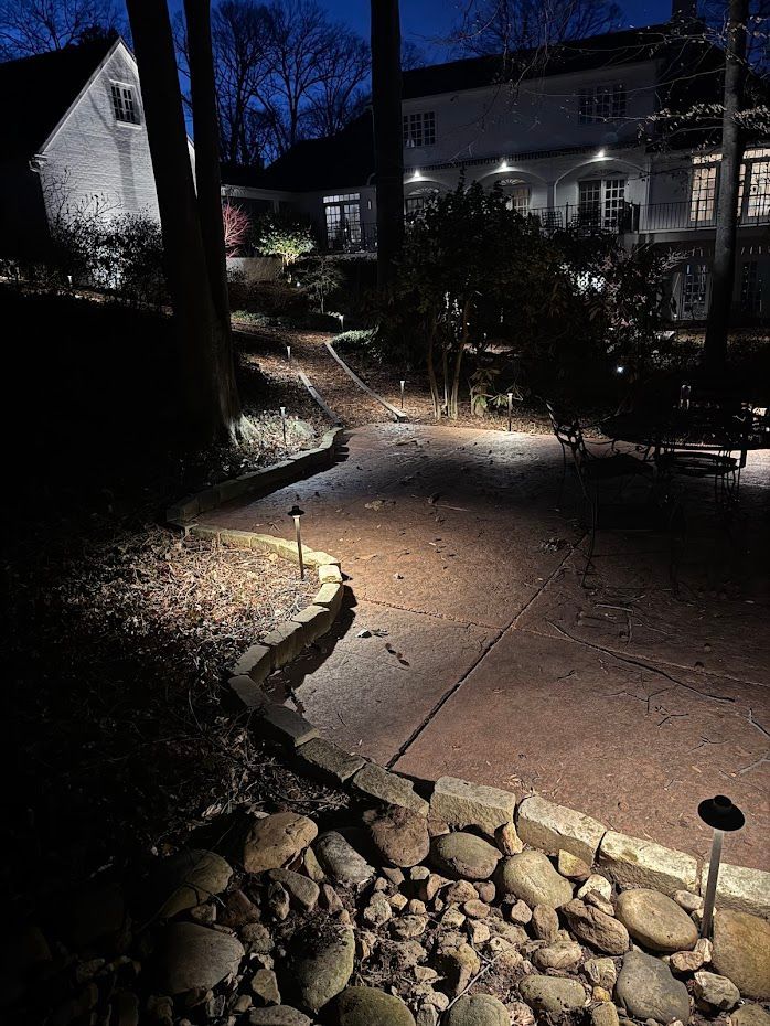 Pathway illuminated by landscape lights at dusk, leading up to a large house.
