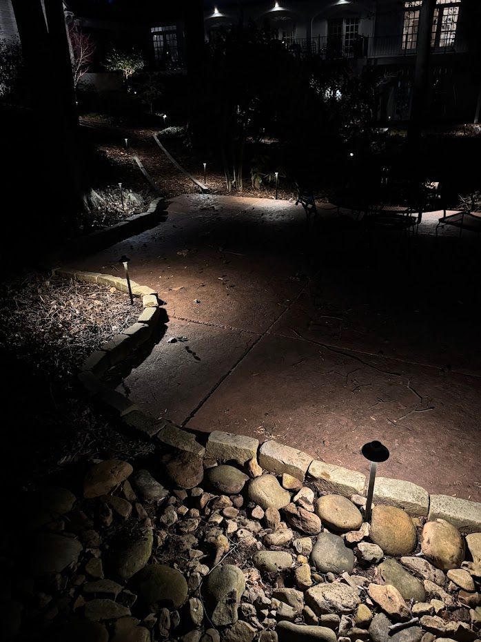 Pathway at night with outdoor lights illuminating the path and rock border, leading to a house in the background.