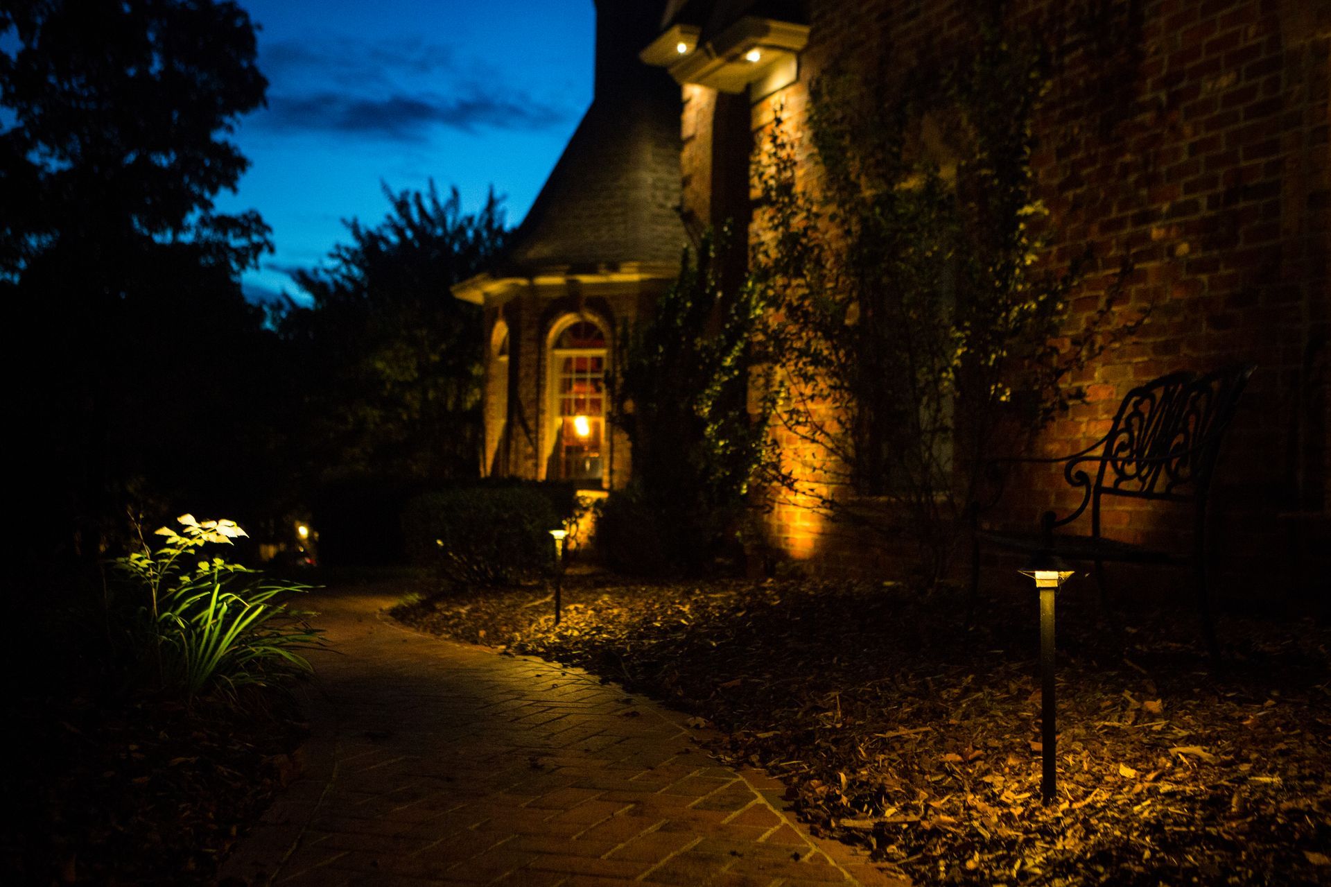 Pathway lit by garden lights leading to a house entrance at dusk.