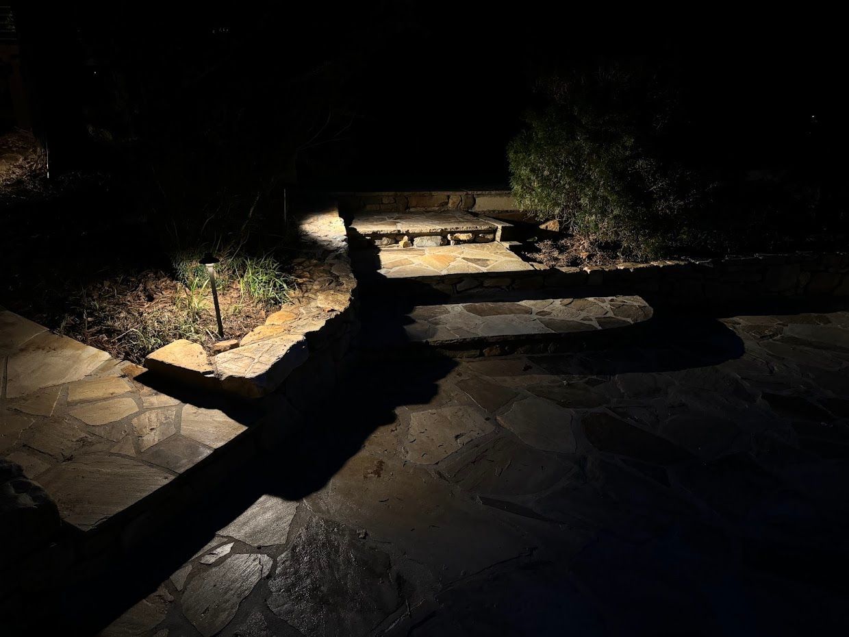 A dark outdoor scene with stone path and steps lit by landscape lighting. A long shadow of a hand is cast.