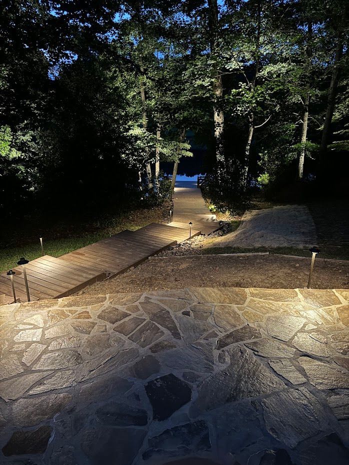 Stone steps and path illuminated by lights lead to a lake at dusk, surrounded by trees.