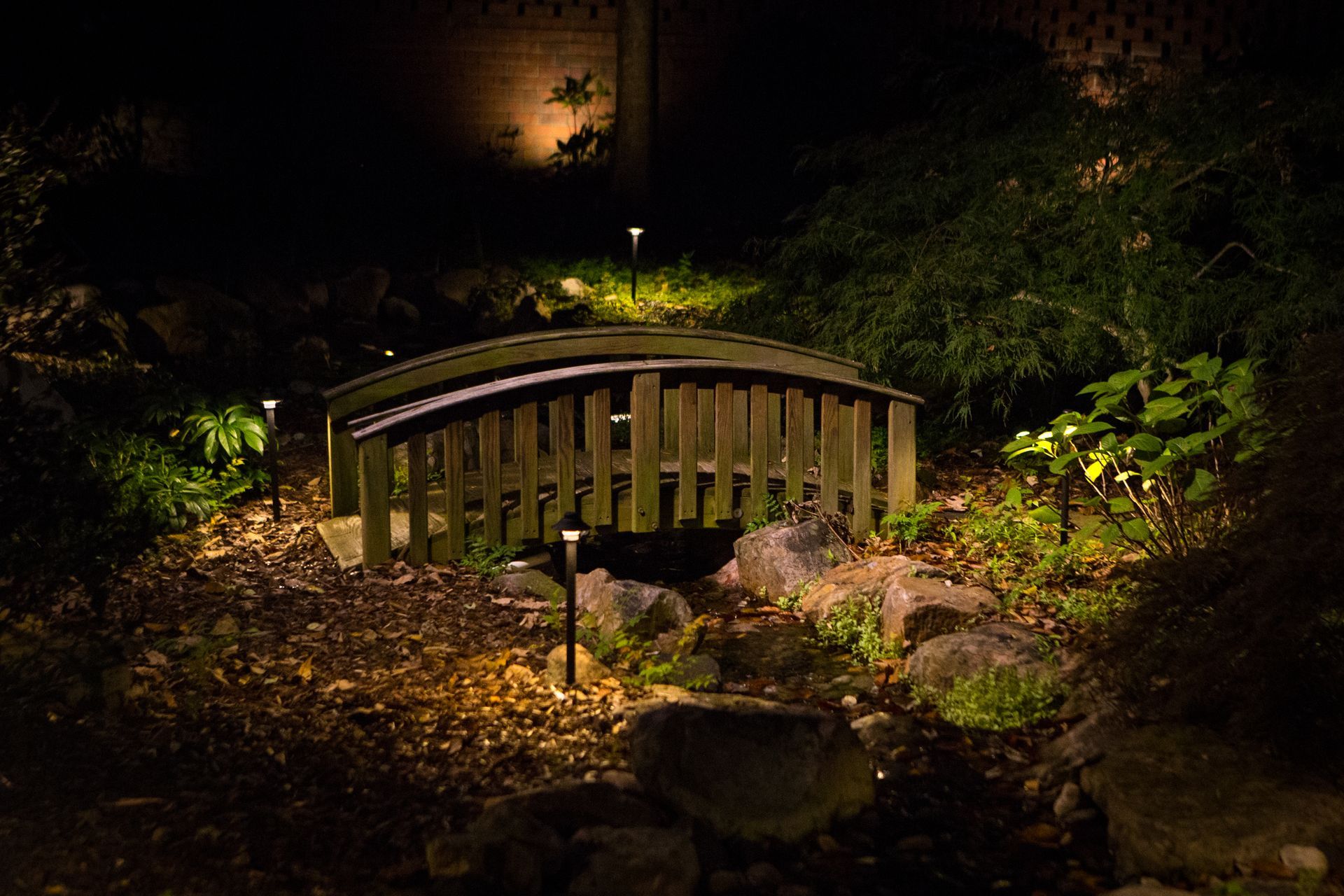 Wooden bridge illuminated by landscape lighting at night.