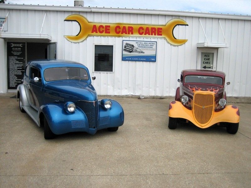 Two old cars are parked in front of ace car care