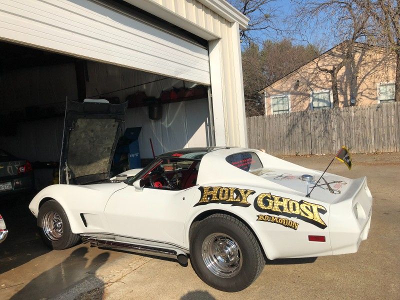 A white corvette is parked in a garage with the door open.