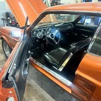 The inside of an orange mustang with the door open and the hood up.