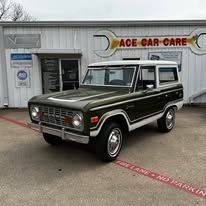 A green bronco is parked in front of a car care shop.