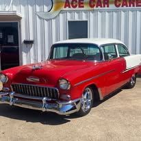 A red and white classic car is parked in front of a car dealership.