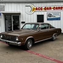 A brown car is parked in front of a car dealership.