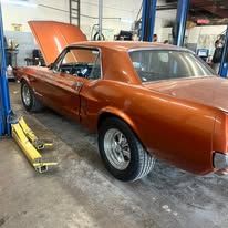 A red mustang is parked in a garage with the hood up.