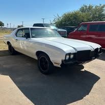 A white car is parked in a parking lot next to a red van.