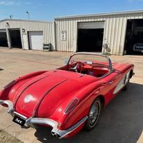 A red corvette convertible is parked in front of a garage.