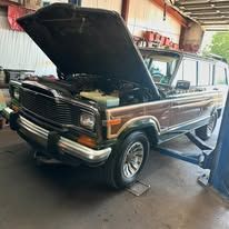 A brown jeep with the hood up is parked in a garage.