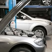 A silver car with its hood open in a garage.